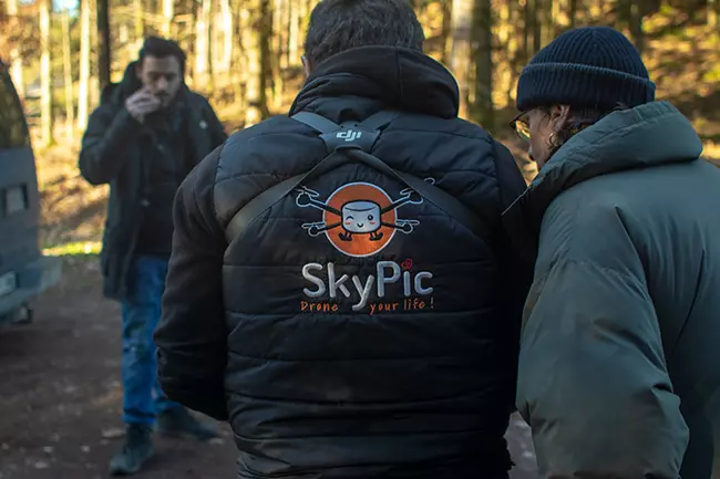 Deux hommes debout dans une zone boisée avec le logo skypic sur leur veste.