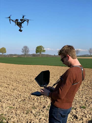 Un homme pilote un drone au-dessus d’un champ.